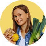 Nathalie Majcher tenant un citron et du gingembre, avec des légumes verts dans les bras.
